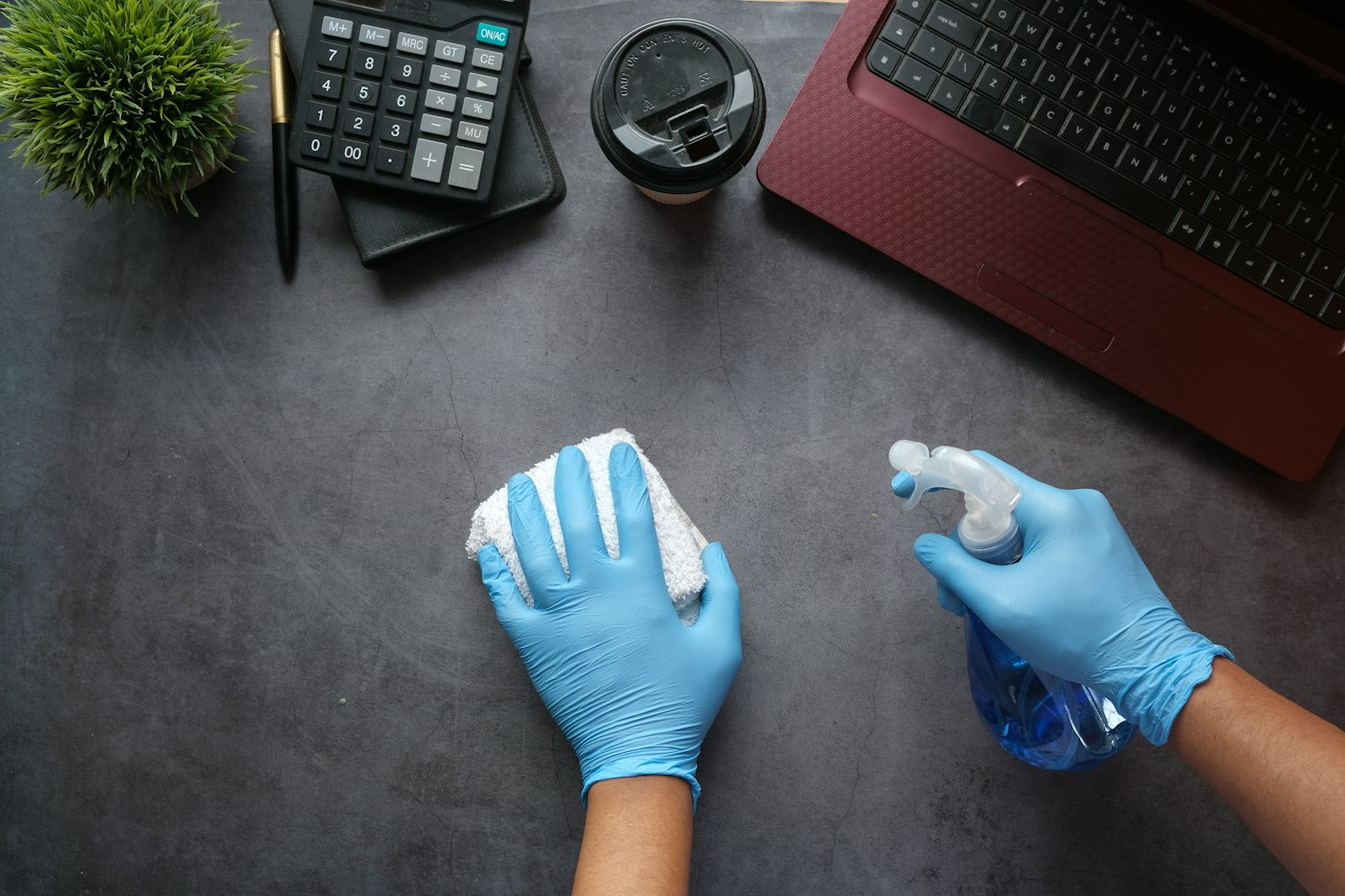 Wiping down an office desk with gloves and spray
